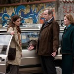Three characters beside a car in front of a graffiti wall