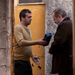 Two men at a doorway exchanging an object